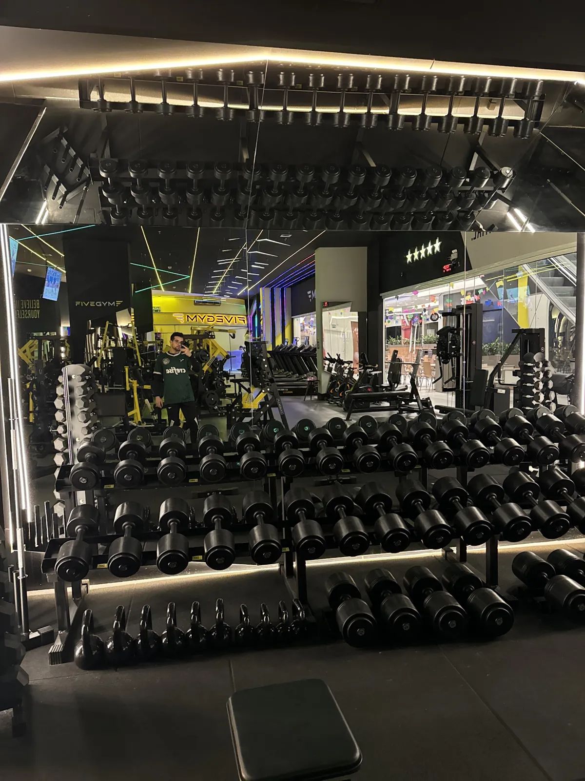 Área de pesos livres da Five Gym com halteres e luz amarela